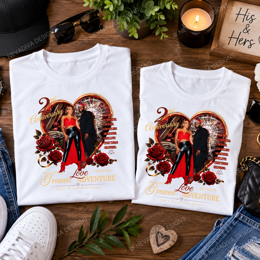 Two folded white anniversary T-shirts displayed on a wooden surface with lifestyle props including sunglasses, a candle, a hat, jeans, a shoe, and a small heart-shaped charm. Each shirt features a large printed graphic of a couple inside a heart with red roses and gold text reading '2nd Anniversary' and 'Love Greatest ADVENTURE'.