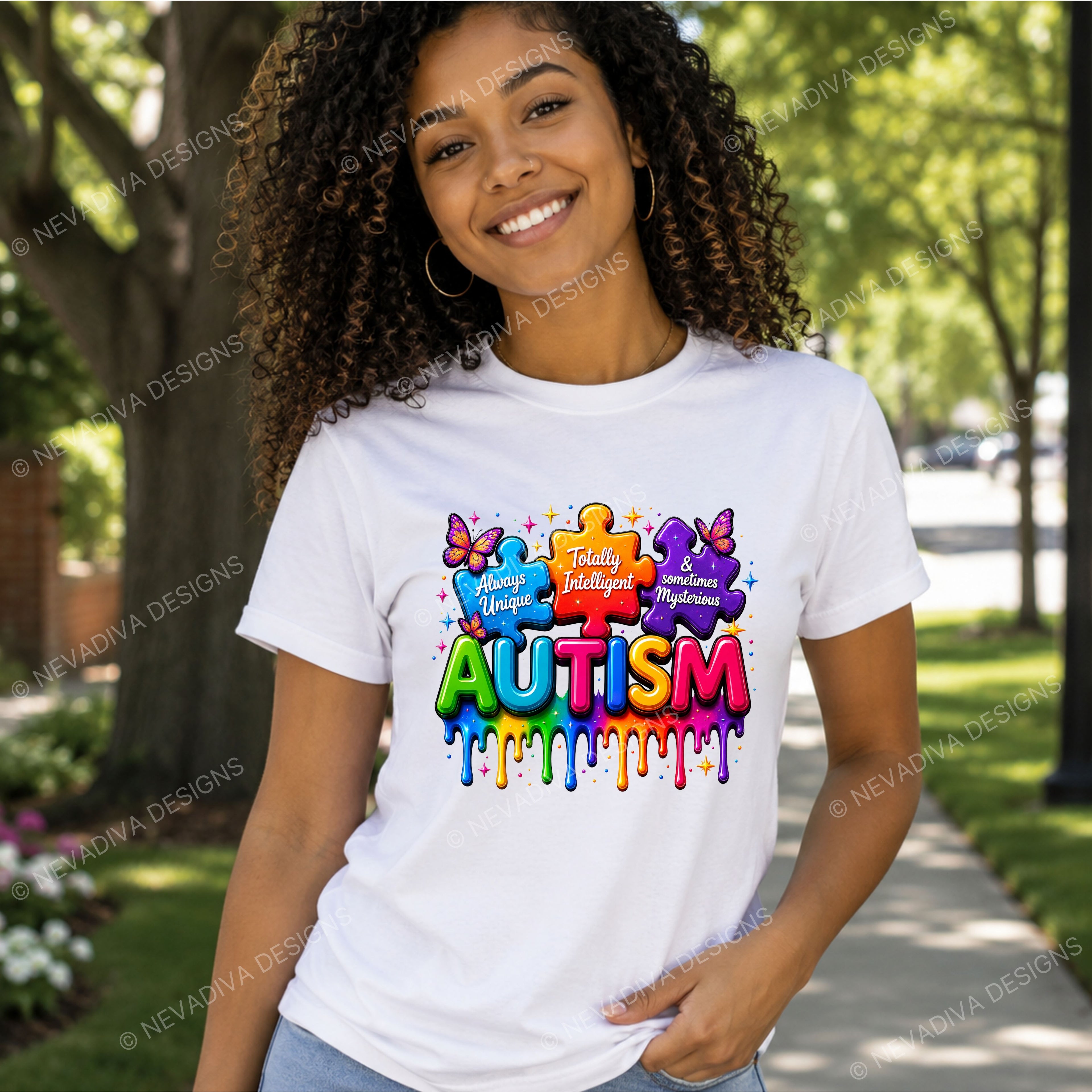 A smiling woman with curly hair stands outdoors on a sidewalk wearing a white graphic T-shirt. The shirt features a colorful autism-themed design with puzzle pieces and the word 'AUTISM' in bright multicolor letters.