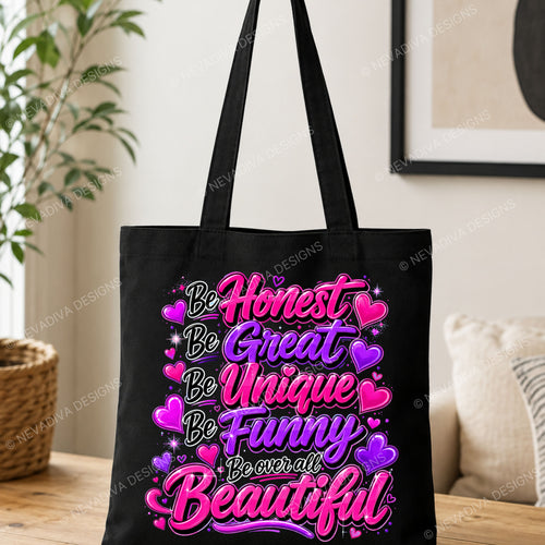 A black canvas tote bag with long handles, featuring a colorful graphic print with the words 'Be Honest Be Great Be Unique Be Funny Be over all Beautiful' in pink, purple, and white lettering with heart accents, set against a blurred indoor background.