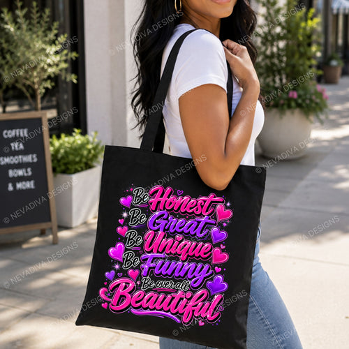 A woman carrying a black canvas tote bag with colorful text that reads 'Be Honest Be Great Be Unique Be Funny Be over all Beautiful' surrounded by pink and purple hearts, set in an outdoor cafe environment.