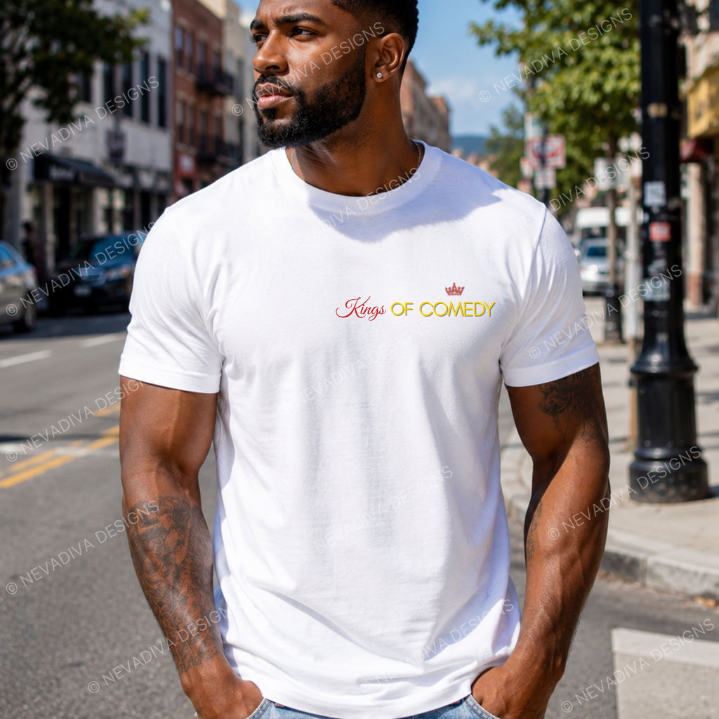 A man wearing a white crewneck t-shirt with 'Kings OF Comedy' printed in red and gold on the chest, standing on a city street.