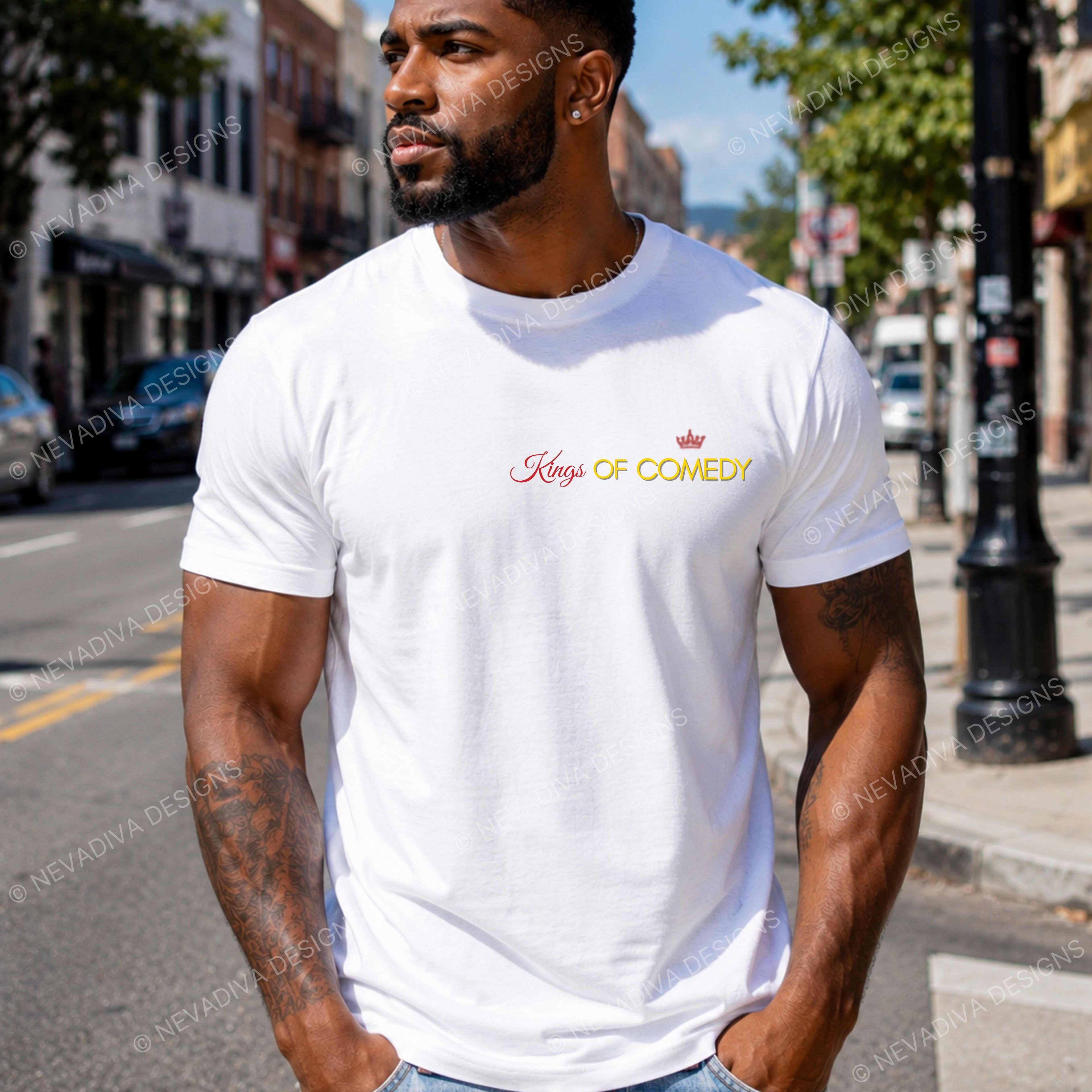 A man wearing a white crewneck t-shirt with 'Kings OF Comedy' printed in red and gold on the chest, standing on a city street.