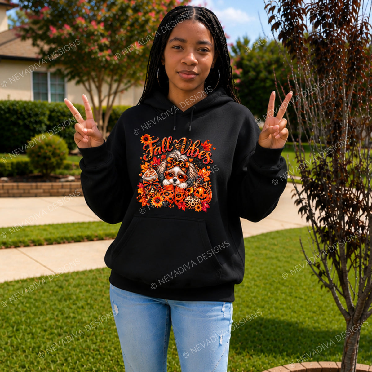 A woman stands outdoors on a lawn wearing a black hoodie with a colorful 'Fall Vibes' graphic featuring a dog, pumpkins, and autumn leaves. She is making peace signs with both hands.