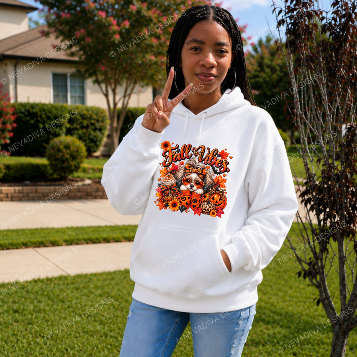 A woman stands outdoors on a lawn wearing a black hoodie with a colorful 'Fall Vibes' graphic featuring a dog, pumpkins, and autumn leaves. She is making peace signs with both hands.