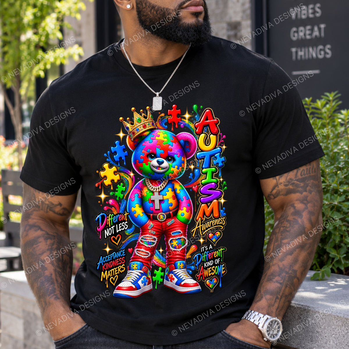 A man wearing a black graphic t-shirt featuring a colorful autism awareness teddy bear design with the text 'Praise Not Less Autism Awareness It's a DIFFERENT kind of awesome'.