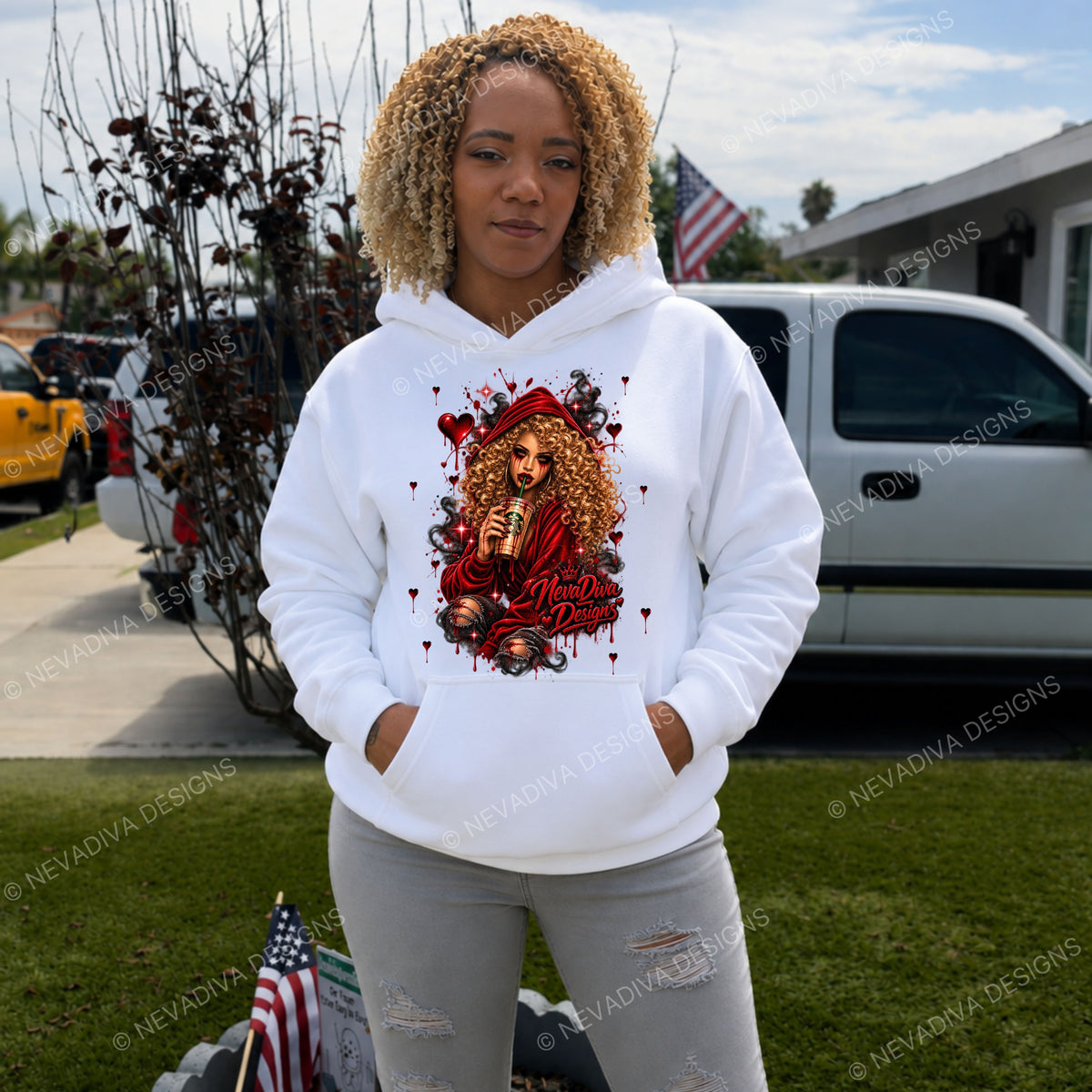 A woman wearing a white pullover hoodie with a large red and gold graphic print of a woman holding a COFFEE, with the NevaDiva Design Logo standing in a residential driveway with a white pickup truck and grass in the background.