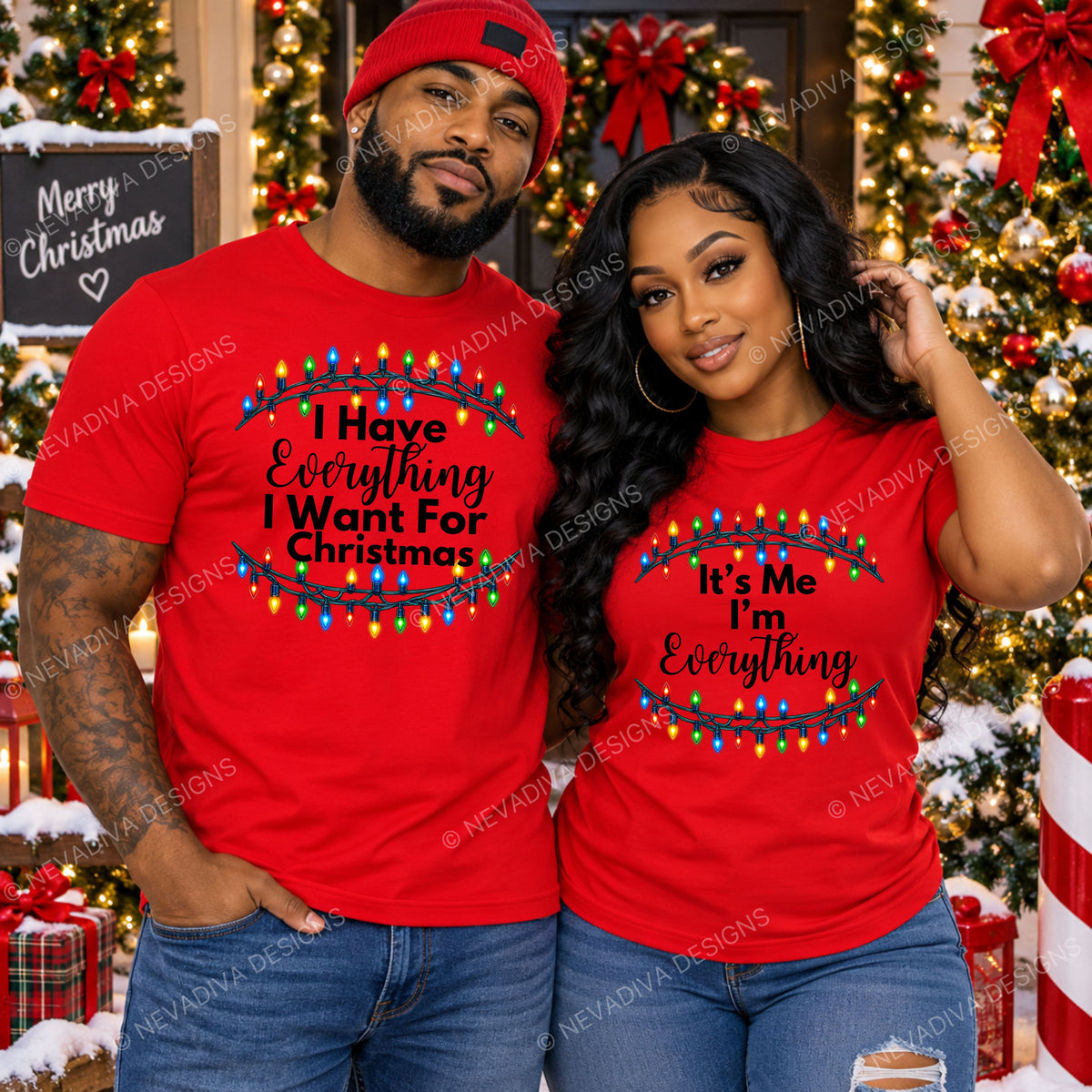 A man and a woman wearing matching red Christmas t-shirts with black text and colorful light bulbs, posed in front of decorated Christmas trees and gifts. The man's shirt reads 'I Have Everything I Want For Christmas' and the woman's shirt reads 'It's Me Everything'.