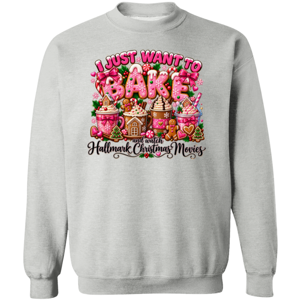 A light gray crewneck sweatshirt featuring a colorful graphic print on the front. The graphic displays the text 'I JUST WANT TO BAKE' in pink and white icing-style lettering above an illustration of hot cocoa mugs, gingerbread houses, and cookies, with the phrase 'and watch Hallmark Christmas Movies' written below in black script.