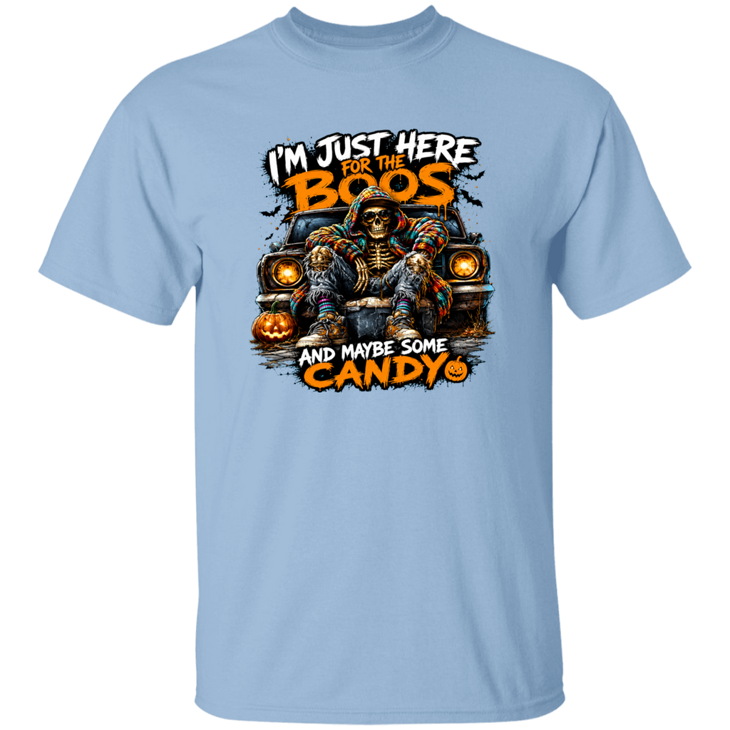 A light blue short-sleeve crewneck t-shirt featuring a Halloween graphic of a skeleton in a casket on a car with jack-o'-lanterns. The text reads 'I'M JUST HERE FOR THE BOOS AND MAYBE SOME CANDY'.