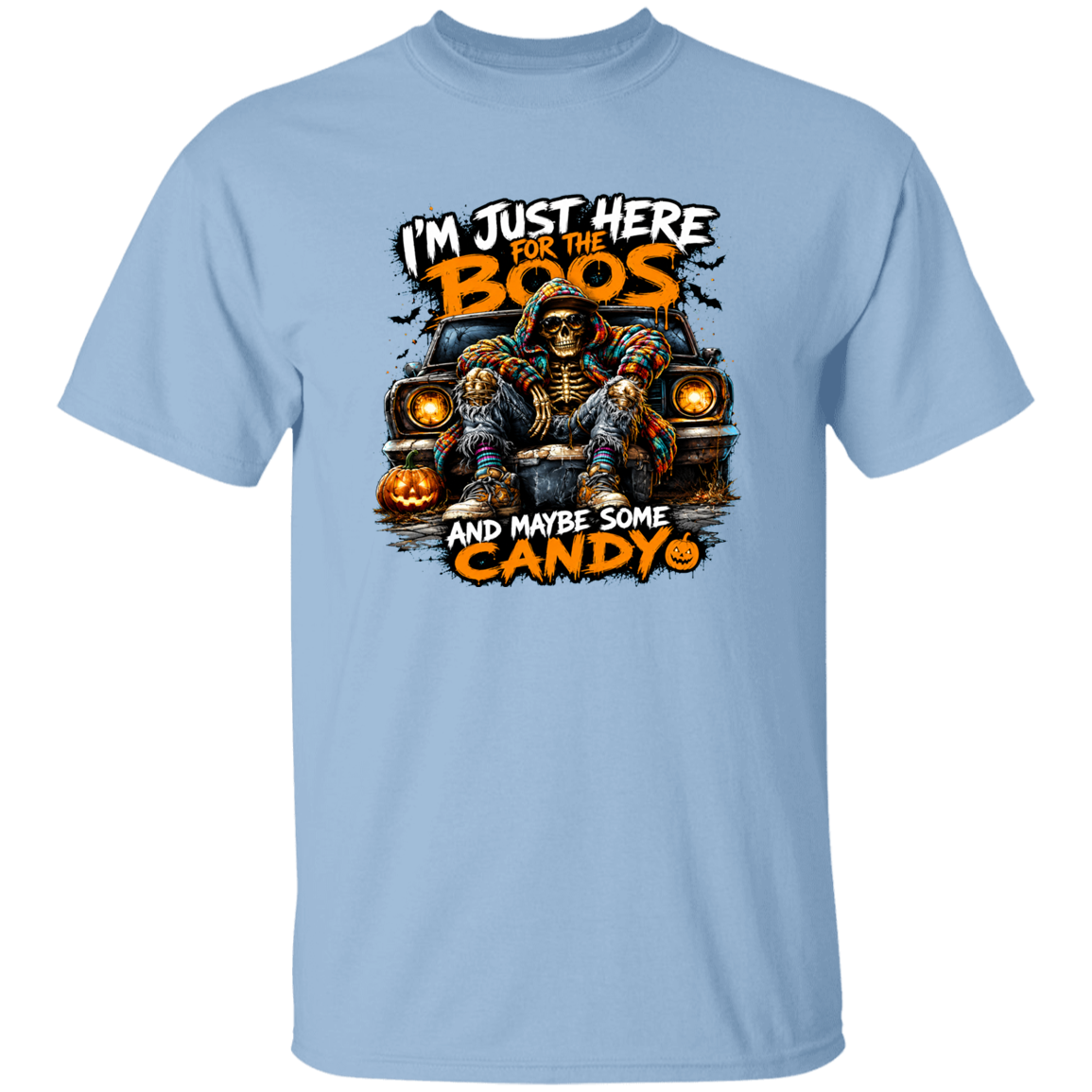 A light blue short-sleeve crewneck t-shirt featuring a Halloween graphic of a skeleton in a casket on a car with jack-o'-lanterns. The text reads 'I'M JUST HERE FOR THE BOOS AND MAYBE SOME CANDY'.