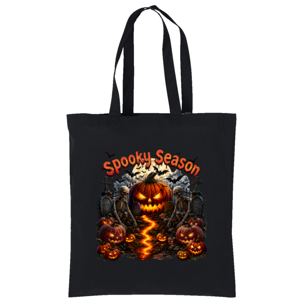 A black canvas tote bag with long black handles, featuring a Halloween graphic print on the front. The design includes the text 'Spooky Season' in orange, a glowing jack-o'-lantern pumpkin, smaller pumpkins, tombstones, bats, and a winding orange flame-like path.