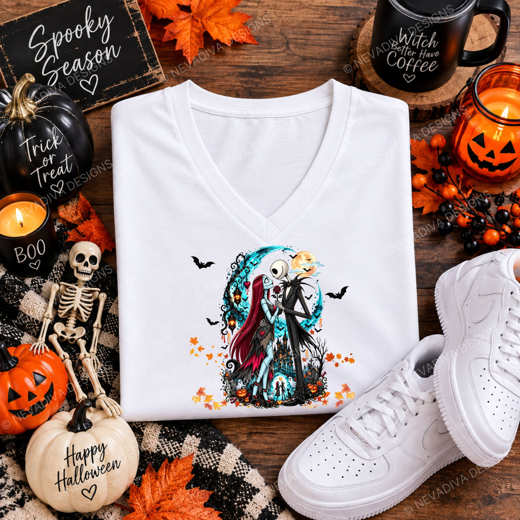 A white V-neck t-shirt with a colorful graphic of Jack Skellington and Sally from The Nightmare Before Christmas, styled in a flat lay with Halloween props including a skeleton, pumpkins, an 'Happy Halloween' pumpkin, a black mug reading 'Witch Coffee', and white sneakers on a rustic wooden background.
