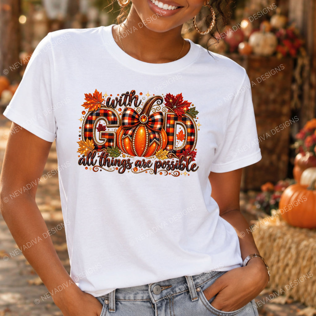 A woman wearing a white graphic t-shirt with a fall-themed design that reads 'with GOD all things are possible' in orange, red, and black plaid lettering, set against an autumn outdoor background.