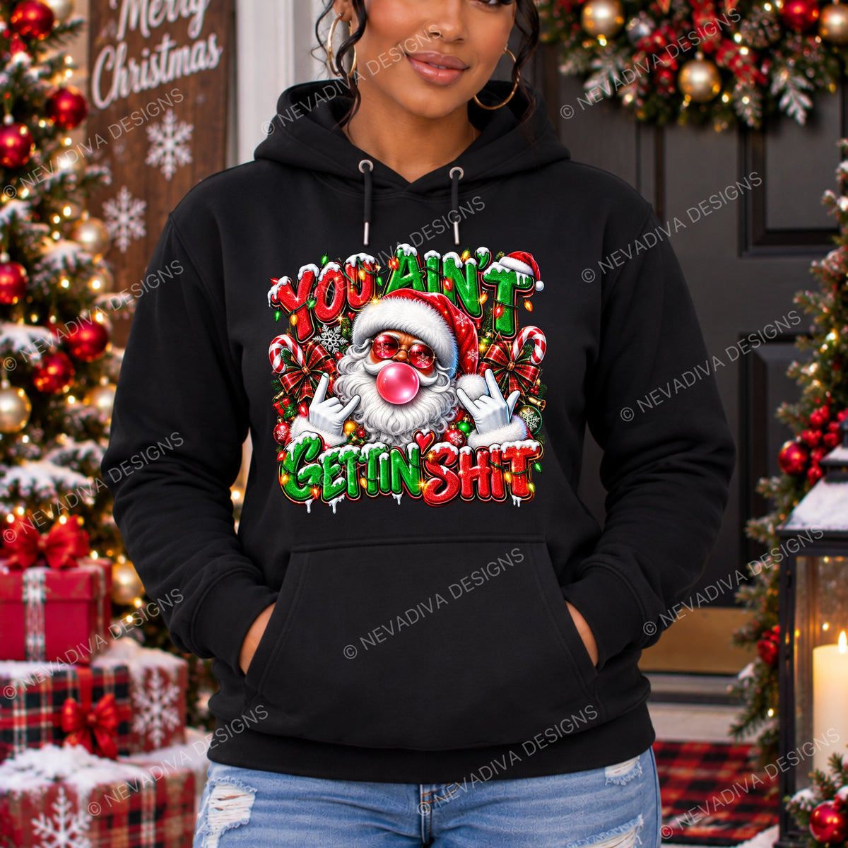 A woman wearing a black pullover hoodie with a colorful Christmas graphic that reads 'YOU AIN'T GETTIN SHIT' and shows a Santa face with a pink nose. The background is a festive Christmas tree decorated with red ornaments and lights.