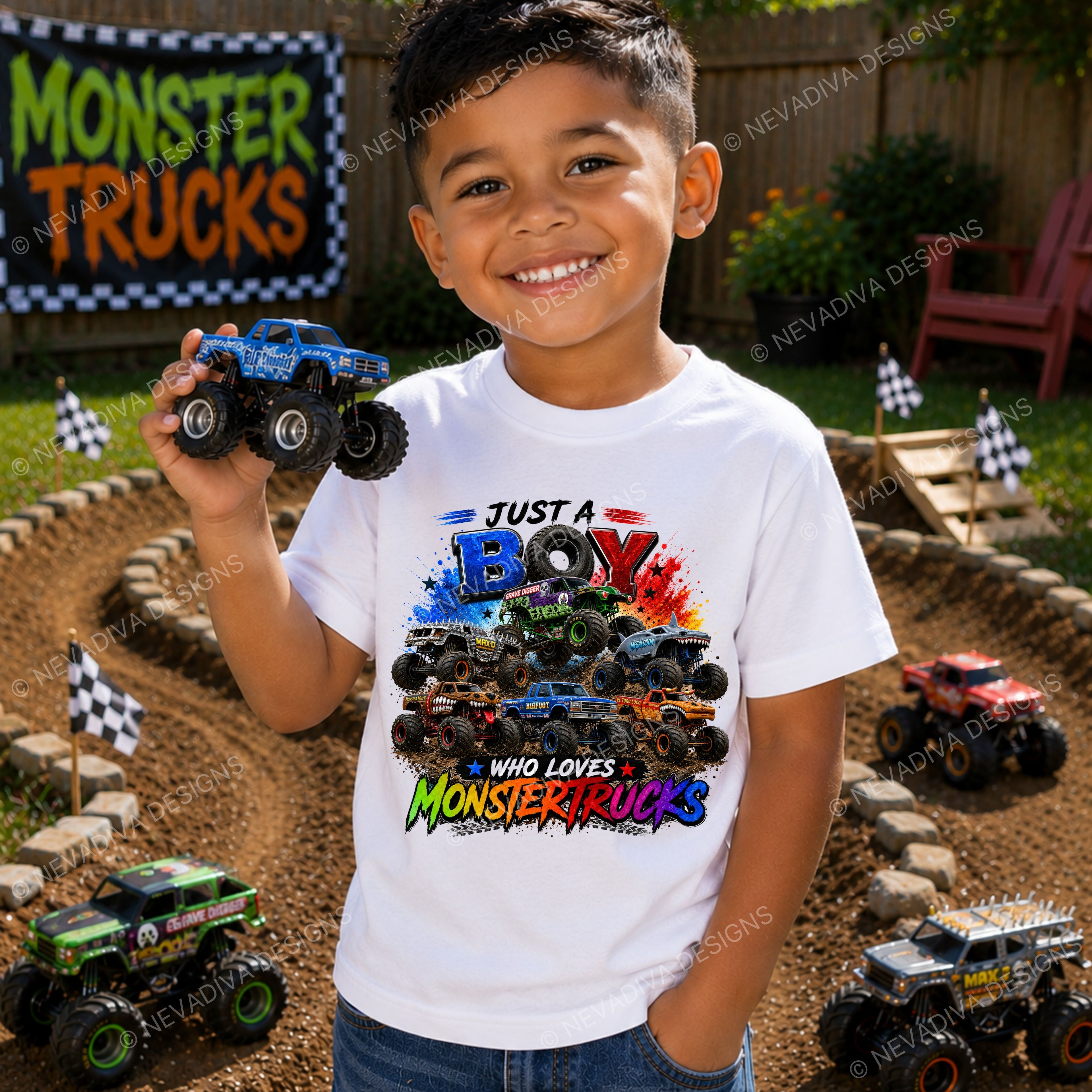 A young boy stands in a backyard setting wearing a white graphic t-shirt with a colorful monster truck print. He is holding a blue monster truck in his hand, with toy monster trucks and a 'Monster Trucks' sign visible in the background.
